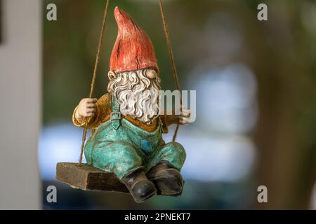 Una figurina di uno gnomo da giardino appeso dall'alto che oscilla su un'altalena di legno Foto Stock