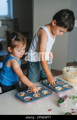 I bambini con le mani spruzzano i cupcakes con il cioccolato. Concetto famiglia felice. Concetto di panetteria per famiglie Foto Stock