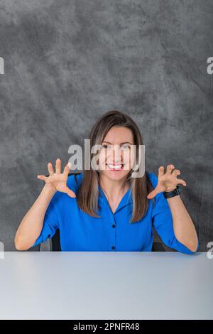 una donna aggressiva in una camicia blu si siede Foto Stock