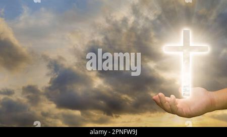 Immagine concettuale di una croce cristiana su una mano umana sullo sfondo del cielo del tramonto Foto Stock