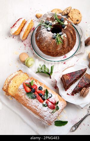 Tavolo da dessert con vari tipi di torte, pezzetti di torte, dolci, biscotti con condimenti di frutta su sfondo bianco. Vista dall'alto. Foto Stock