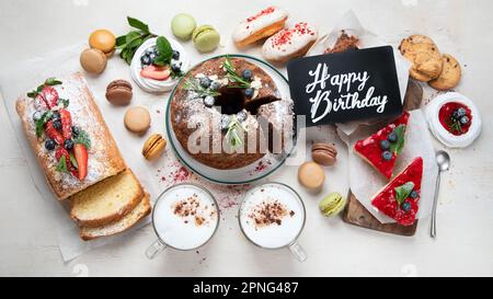 Tavolo da dessert con vari tipi di torte, pezzetti di torte, dolci, biscotti con condimenti di frutta su sfondo bianco. Vista dall'alto. Foto Stock