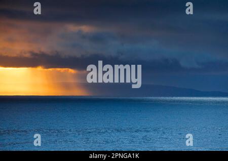 Il sole serale si interrompe attraverso le basse nuvole di pioggia sopra le Isole Summer e le acque aperte dell'Atlantico blu, costa occidentale della Scozia Foto Stock