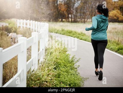 Fai il pieno di allenamento. Ripresa da dietro di una giovane donna che va per una corsa in natura. Foto Stock