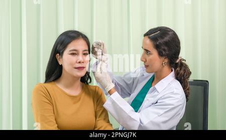 Il medico in abito bianco e guanto protettivo si prepara a somministrare un'iniezione a una paziente femmina. Foto Stock