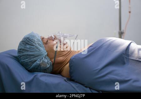 Paziente asiatico anziano che respira con respiratore, sdraiato sul letto dell'ospedale in sala operatoria in attesa di un intervento chirurgico. Foto Stock