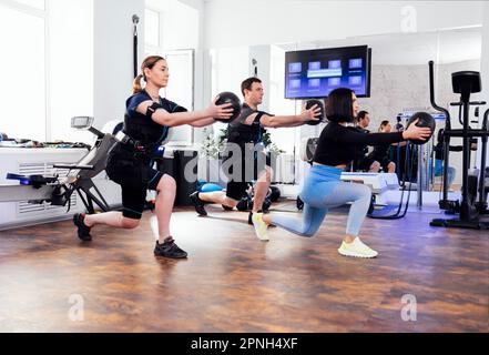 Sport Couple in ems si allenano con personal trainer in palestra. I giovani tengono speciali palle mediche ponderate in mani distese. Uomo e donna Foto Stock