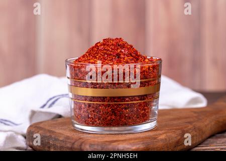 Peperoncino rosso. Peperoncino schiacciato o scaglie di peperoncino essiccato in una ciotola di vetro su fondo di legno Foto Stock