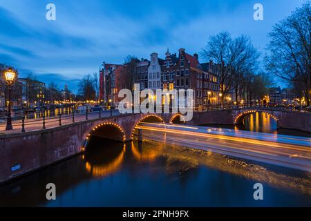 Ponti illuminati al crepuscolo ora blu ad Amsterdam, Olanda, Paesi Bassi nel mese di aprile - lunga esposizione con luci di barca che passano sotto il ponte Foto Stock