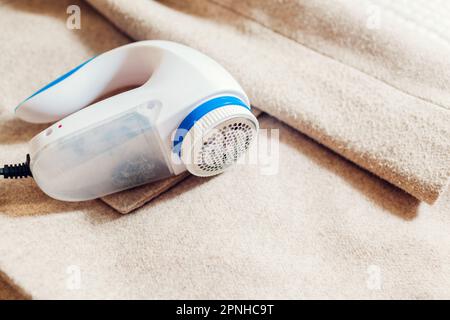 Primo piano del dispositivo per la rimozione del pelucco cablato. Pulire i vestiti con un rasoio elettrico a fusione a casa. Rasatura del pilling dal cappotto con una macchina moderna Foto Stock