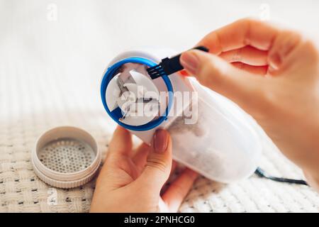 Donna che pulisce il rasoio per rimuovere il pelucchi dopo aver rasato il filo utilizzando una piccola spazzola. Contenitore pieno di pilling rifinito e sporcizia. Primo piano del dispositivo Foto Stock