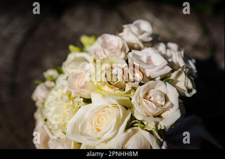 Un paio di anelli d'oro su un moncone, un bouquet di fiori della sposa sullo sfondo Foto Stock