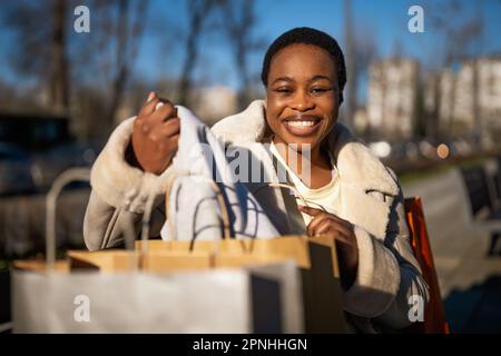 Ritratto all'aperto di felice donna nera. Lei è seduta su panca in strada dopo lo shopping. Foto Stock