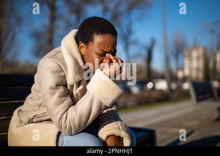 Ritratto all'aperto di stanca donna nera in giornata di sole. Sta avendo mal di testa. Foto Stock