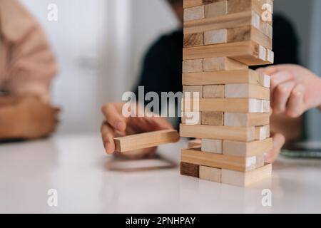 Mani di primo piano di un uomo irriconoscibile rimuovendo con attenzione il blocco di legno dalla torre instabile impilata durante il gioco con gli amici alla festa. Foto Stock