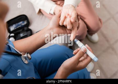 vista dall'alto dell'infermiera multirazziale in penna lancetta in uniforme vicino alla donna anziana Foto Stock