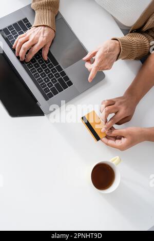 vista dall'alto della donna in pensione che digita sulla tastiera del notebook vicino a un assistente sociale multirazziale con carta di credito Foto Stock