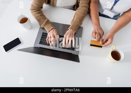 vista dall'alto della donna anziana che digita sulla tastiera del computer portatile vicino a un assistente sociale multirazziale con carta di credito Foto Stock
