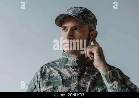 soldato in uniforme e cuffia regolabile auricolare wireless isolato sul grigio Foto Stock