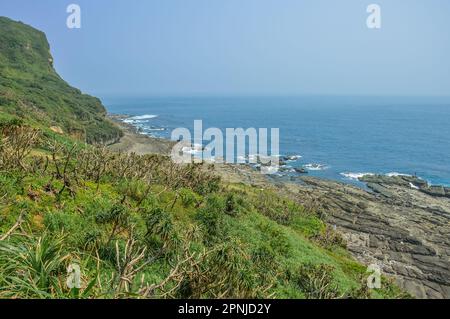 Montagna verde naturale sulla spiaggia rocciosa con acqua di mare blu di Capo Bitou (Bitoujiao) nel quartiere Ruifang della città di New Taipei, Taiwan Foto Stock