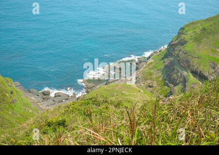 Montagna verde naturale sulla spiaggia rocciosa con acqua di mare blu di Capo Bitou (Bitoujiao) nel quartiere Ruifang della città di New Taipei, Taiwan Foto Stock