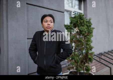 donna multirazziale con problema mentale in piedi vicino alla costruzione sulla strada urbana, immagine di riserva Foto Stock