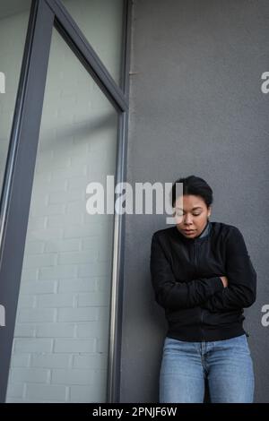 Giovane donna multirazziale con apatia in piedi vicino edificio all'aperto, immagine stock Foto Stock