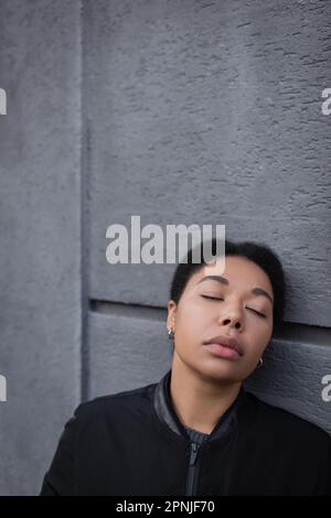 Giovane donna multirazziale con depressione in piedi vicino a edificio all'aperto, immagine stock Foto Stock