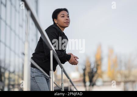 donna multirazziale con problema mentale guardando via mentre in piedi vicino ringhiera sulla strada, immagine di riserva Foto Stock