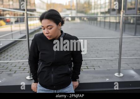 donna multirazziale con problema mentale in piedi vicino ringhiera su strada urbana, immagine di riserva Foto Stock