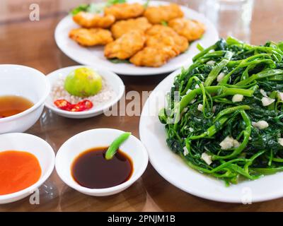 Vietnamita fritto mattina gloria, rau muong xao toi, e dolci vietnamiti di pesce, cha ca quy nhon, fuori fuoco in background. Fritto mattina gloria è Foto Stock