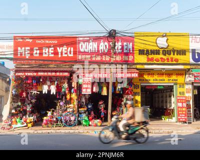 Negozio di giocattoli e negozio di telefonia mobile in un villaggio a Thai Binh, Vietnam. Moto che passa in primo piano sfocato a causa della velocità. Foto Stock