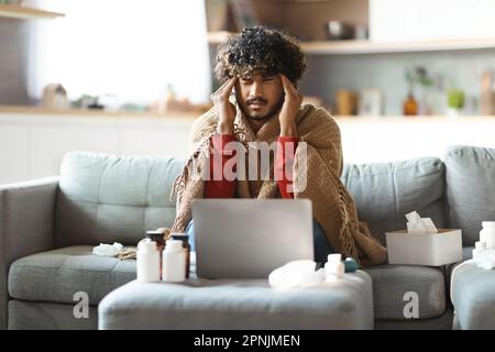 Uomo indiano malato coperto in coperta seduta sul lettino a casa Foto Stock