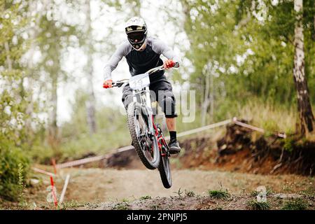 il pilota di mountain bike in discesa salta sopra il trampolino nella corsa del sentiero nella foresta Foto Stock