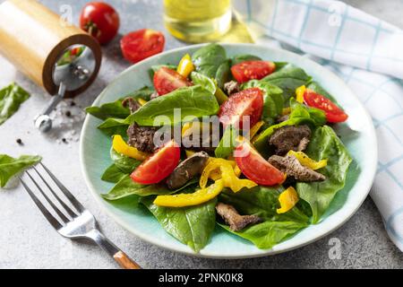 Insalata calda di spinaci giovani, fegato di pollo, pomodori e peperoni alla griglia con spezie e balsamico. Dieta sana cheto basso carb. Foto Stock