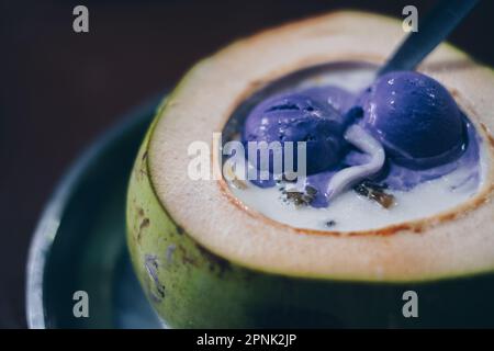 Primo piano del famoso dessert filippino, le soste di ghiaccio rasate AKA Halo-Halo in conchiglia di cocco o buko con due cucchiai di gelato al cubetto in cima. Messa a fuoco selezionata. Foto Stock