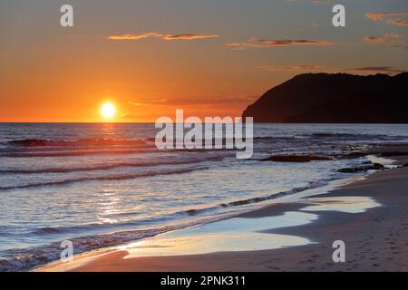 Tramonto sulla costa del Parco naturale di Calblanque, Cartagena, regione di Murcia, con onde morbide che lavano la riva e la sagoma delle scogliere. Foto Stock