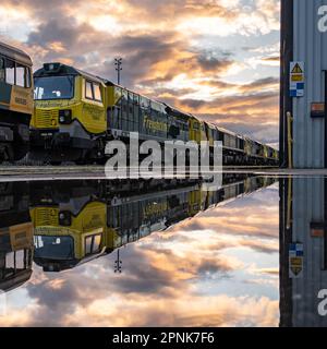 LEEDS, REGNO UNITO - 12 APRILE 2023. Una linea di locomotive Freightliner di classe 70 al tramonto nel deposito di manutenzione di Leeds, riflesse nell'acqua Foto Stock