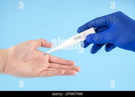 Il medico in guanti di lattice blu passa il termometro digitale nelle mani del paziente. Misurazione della temperatura corporea. Foto Stock