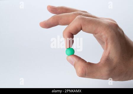 Mano maschile che tiene una pillola verde su uno sfondo grigio. Primo piano Foto Stock