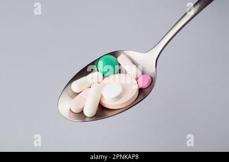 Compresse, compresse e capsule assortite di medicinali farmaceutici su un cucchiaio di metallo Foto Stock