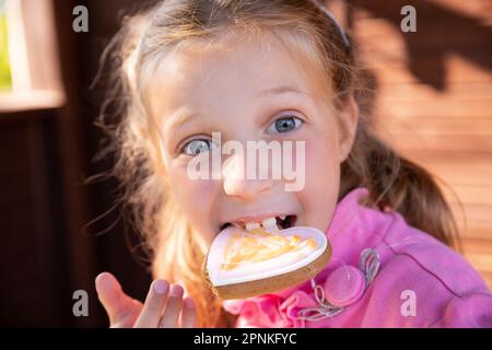 Ragazza sorridente teen mangiare biscotti di farina d'avena su sfondo sfocato.ragazza bionda felice mangiare pan di zenzero a casa Foto Stock