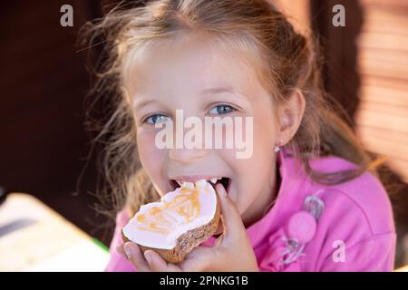 Ragazza sorridente teen mangiare biscotti di farina d'avena su sfondo sfocato.ragazza bionda felice mangiare pan di zenzero a casa Foto Stock