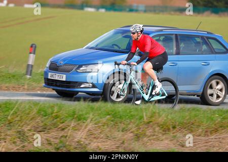Un ciclista che viene sormontato da un veicolo a motore sulla B1222 vicino a Sherburn-in-Elmet, North Yorkshire, UK Foto Stock