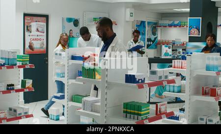 Farmacista afroamericano mettere farmaci in scaffali in farmacia, organizzare scatole di farmaci e integratori. Lavoratore di farmacia che organizza pillole e vitamine nel negozio al dettaglio. Foto Stock