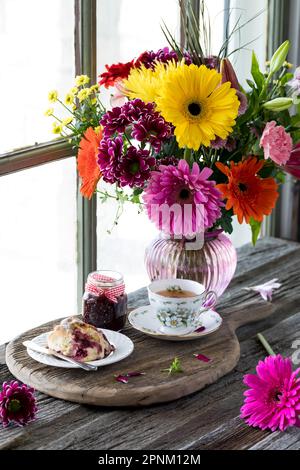 Una bella composizione floreale con tè e scone di fronte, su una tavola rustica. Foto Stock