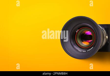 Obiettivo anteriore della telecamera vintage con corpo nero isolato su sfondo giallo o arancione con spazio copia. Foto Stock