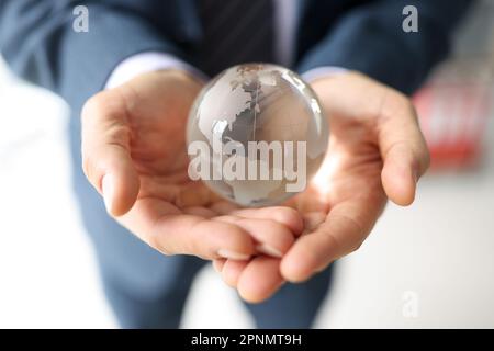 Uomo in tuta da lavoro tiene globo di vetro con continenti Foto Stock