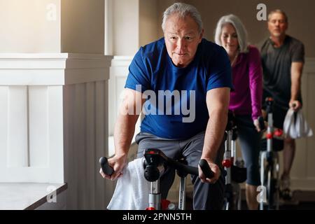 Gli anziani lo stanno facendo per se stessi. un gruppo di anziani che hanno una lezione di spinning in palestra. Foto Stock