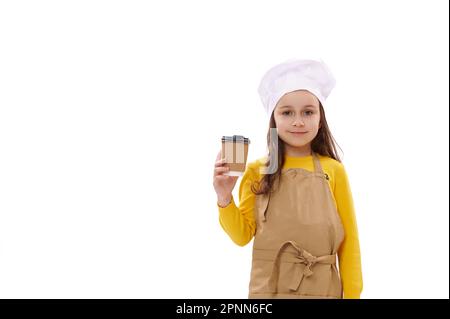 Ragazza caucasica in cappello dello chef e grembiule da cucina, tiene bevande da asporto in tazza di carta usa e getta. Servizio di consegna cibo Foto Stock